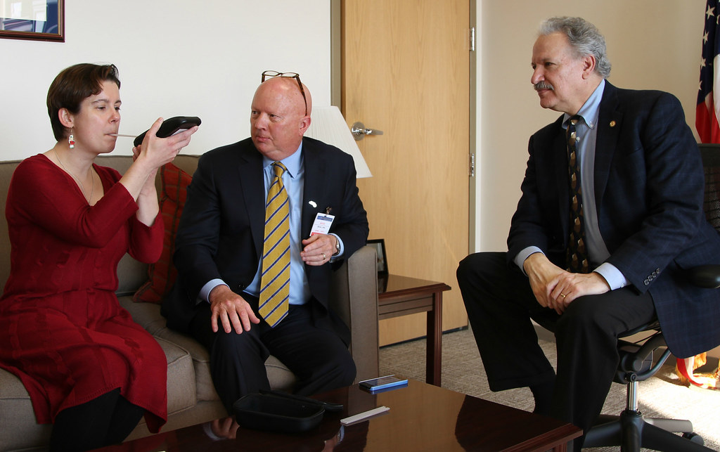 A specialist demonstrates a handheld alcohol monitoring device to two officials.